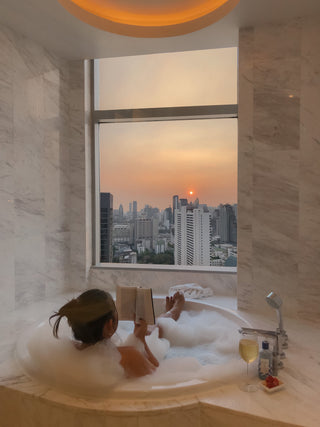 A woman embracing her soft life - a relaxing bubble bath, box, wine and city sunset