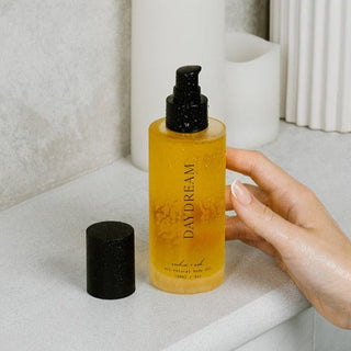 Hand holding a bottle of 'Daydream' body oil on a light surface.