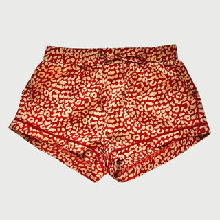Close up of red and gold leopard print pajama shorts on a plain grey background.