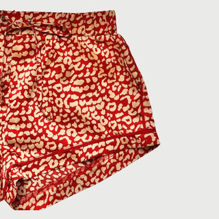 Close up of a half section of red and gold leopard print pajama shorts on a plain white/grey background.