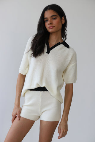 Woman wearing summery white knit short sleeve polo with black collar detailing