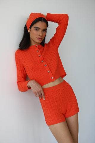 Woman wearing cable-knit lounge shorts in red poppy color with a soft, cozy texture and matching cardigan