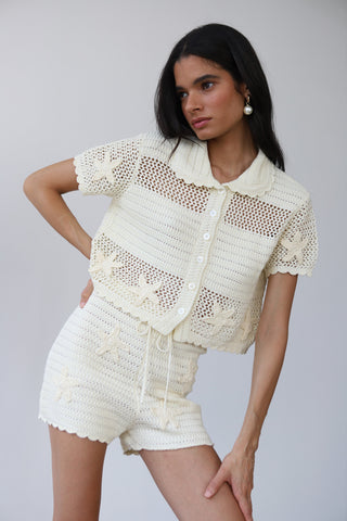 Woman wearing white lightweight crochet knit button up with matching knit shorts