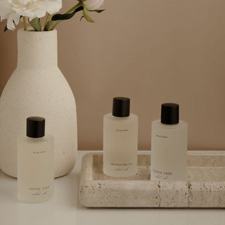 Three bottles of Hippie Soul natural body and room spray on a stone tray with a vase of flowers in the background.