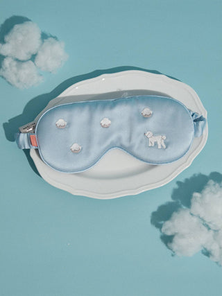 Blue sleep mask with cloud and dog pattern on a light blue background