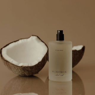 Moonstruck ritual spray bottle with a split coconut on a reflective surface