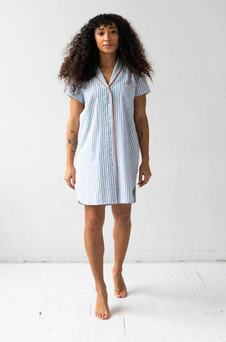 Woman wearing short sleeve button down sleep shirt in blue and white stripes with pink trim.