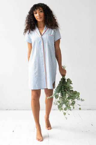 Woman wearing short sleeve button down sleep shirt in blue and white stripes with pink trim.