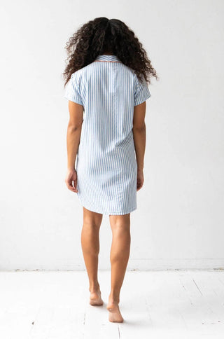 Woman wearing short sleeve button down sleep shirt in blue and white stripes with pink trim.