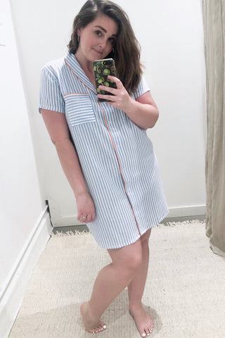 Woman wearing short sleeve button down sleep shirt in blue and white stripes with pink trim.