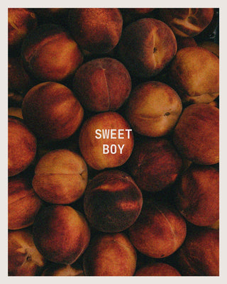 A close-up photo of many ripe peaches filling the frame, with the words 'SWEET BOY' printed in white centered over one peach.